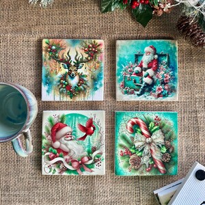 以下が含まれることがあります： お祝いのデザインが施された4つの正方形のクリスマスコースター。1つは花輪のある鹿、もう1つはサンタクロース、3つ目は赤い鳥とサンタクロース、最後はリボン付きのキャンディケーンが特徴です。