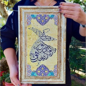 May include: A rectangular wall art piece featuring a central black Arabic calligraphy design of a whirling dervish on a cream-colored stone tile background with blue and gold floral borders, encased in a distressed gold frame, measuring 15 inches by 9.5 inches.