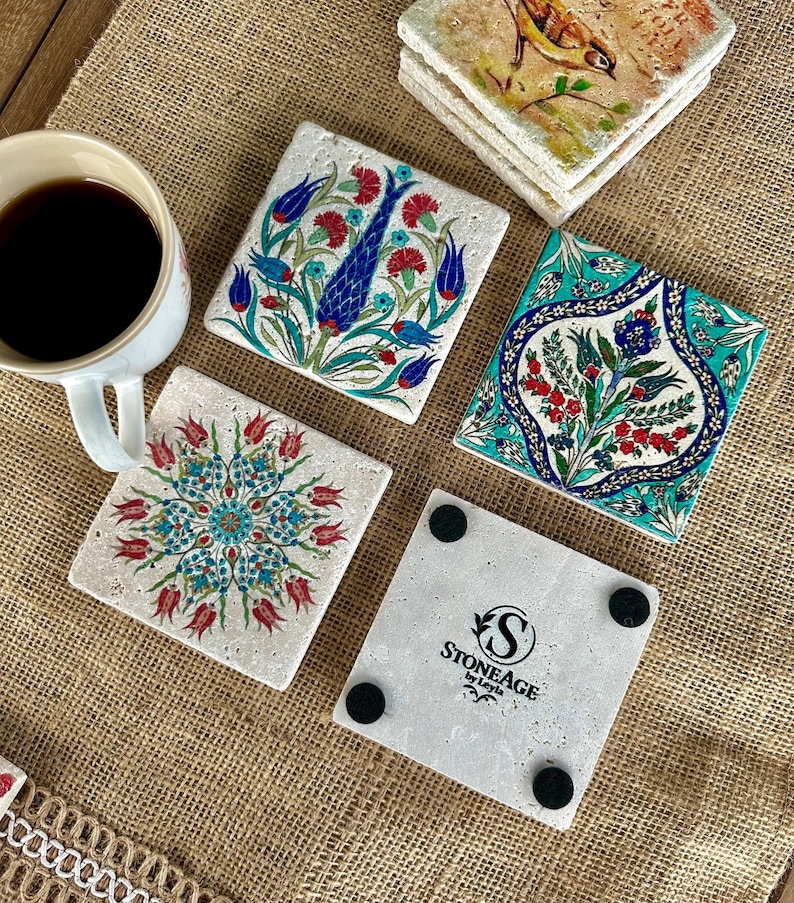 May include: Set of square stone coasters with colorful floral designs. The coasters feature red, blue, and turquoise patterns. One coaster has the text "STONEAGE by Leyla". A white mug with coffee is in the image.