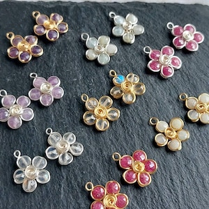 Può includere: Una collezione di ciondoli a forma di fiore realizzati con pietre preziose avvolte in filo metallico. Ogni ciondolo presenta cinque petali di pietra sfaccettata disposti attorno a un nucleo centrale di filo avvolto con un occhiello.