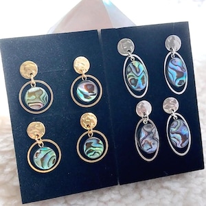 May include: Four pairs of dangle earrings displayed on black cards. Two pairs feature gold-tone hammered discs with circular frames holding round abalone shell cabochons. Two pairs feature silver-tone hammered discs with oval frames holding oval abalone.