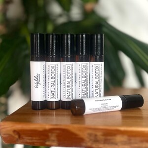 May include: Six small, black and white labeled bottles of face targeting serum called "Natural Botox" on a wooden surface. The bottles are arranged in a row, with the labels facing the viewer. The text on the labels reads "Face Targeting Serum Natural Botox A Natural Retinol for Wrinkles Fine Lines & Firming Skin".