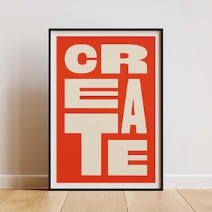 Puede incluir: Un póster enmarcado con la palabra "CREATE" en letras grandes y en negrita de color crema sobre un fondo naranja brillante. El póster está en un marco negro y se muestra en una pared sobre un suelo de madera.