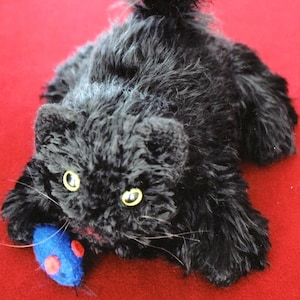 May include: A black plush toy cat with a long, fluffy tail, playing with a blue and red toy mouse. The cat has yellow eyes and a pink nose.