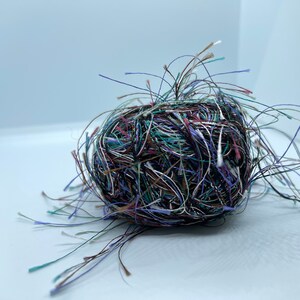 May include: A tangled ball of yarn in shades of brown, green, blue, and white. The yarn is loose and unraveled, with strands extending out in all directions.