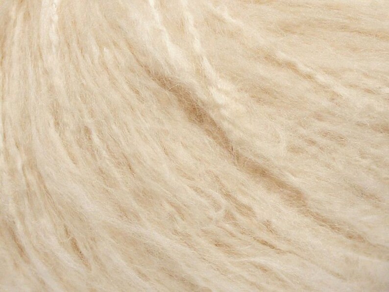 May include: Close-up of a soft, cream-colored yarn. The yarn is made of natural fibers and has a fluffy texture.