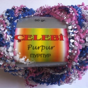 May include: A skein of yarn in pink, white, and blue with silver thread. The yarn is labeled "Celebi Rurpur Purpur" and "50 gr."