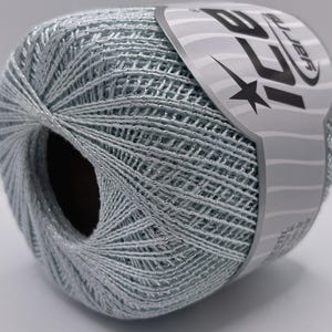 Puede incluir: Ovillo de hilo azul claro con hilo plateado metálico. El hilo está bien enrollado y tiene una etiqueta con la marca "ICE Yarn". Adecuado para proyectos de punto y ganchillo. El diámetro del ovillo es de aproximadamente 10 cm.
