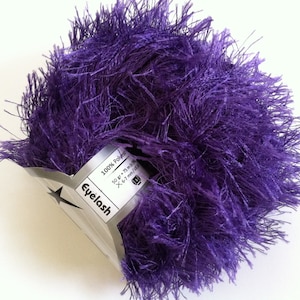 May include: A skein of purple eyelash yarn, 100% polyester, 50 grams, 75 meters, 6-7 mm needles. The yarn is packaged in a silver label with the brand name "Eyelash" printed on it.