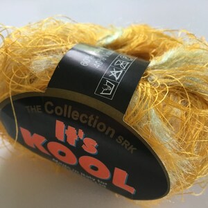 May include: A skein of yellow and pale green It's Kool yarn from The Collection SRK. The yarn is a blend of fibers, with a label wrapped around the center. The label is black with orange and white text, and includes washing instructions.