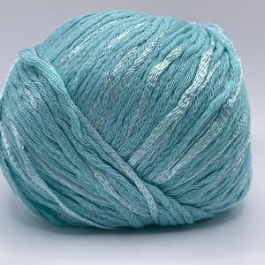 May include: A ball of turquoise yarn with white and silver threads woven throughout. The yarn is tightly wound, showing the texture of the fibers. Ideal for knitting and crochet projects.