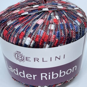 May include: A ball of red, white, and blue yarn with silver accents. The yarn is labeled "Berlini Ladder Ribbon".