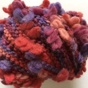 May include: A ball of yarn with a mix of red, pink, and purple colors. The yarn is fluffy and has a textured look.