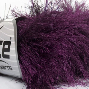 May include: A close-up of a skein of purple Ice Yarns. The yarn is a deep, rich purple color with a feathery texture. The label is silver and white with the brand name "ICE YARNS" in black.