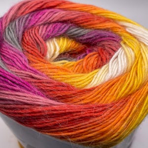 May include: A skein of yarn with a multi-colored ombre pattern. The yarn is a mix of orange, yellow, white, pink, and gray.