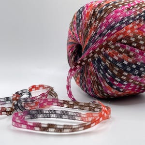 May include: A ball of colorful yarn with a woven texture, featuring shades of pink, orange, brown, and navy blue. A length of the same yarn is unraveled, displaying a checkered pattern. Ideal for crafting and textile projects.