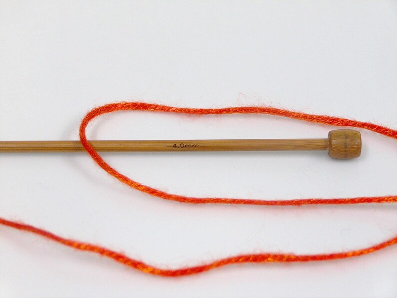 Puede incluir: Primer plano de una aguja de tejer de madera con el texto "4.0mm" y lana naranja brillante. La lana est&aacute; enrollada alrededor de la aguja, lo que sugiere un proyecto de manualidades. La aguja es de madera de color marr&oacute;n claro.