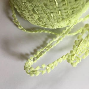 Könnte beinhalten: Nahaufnahme einer hellgrünen Borte mit einer flauschigen Textur. Die Borte hat ein sich wiederholendes Muster aus kleinen Bommeln.