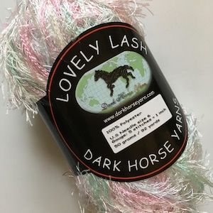 以下が含まれることがあります： ピンク、白、緑の糸の玉で、黒いラベルには「Lovely Lash」と「Dark Horse Yarn」と書かれています。ラベルには、糸の詳細も記載されています。100%ポリエステル、US針サイズ6、ゲージ: 5目 = 1インチ、50グラム / 92ヤード。