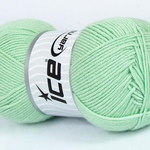 Könnte beinhalten: Ein mintgrüner Wollknäuel mit einem weißen Etikett mit der Marke "ICE yarns". Das Garn ist eng gewickelt und zeigt die Textur der Fasern. Ideal für Strick- und Häkelprojekte.