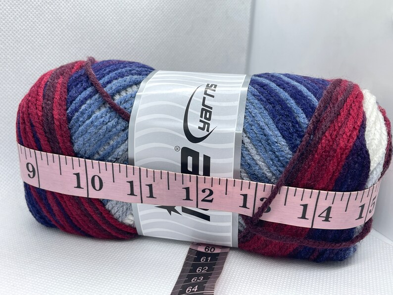 May include: A skein of blue, red, and white yarn with a label that reads "Big Yarns". The yarn is measured with a pink tape measure that reads 9 to 15 inches.