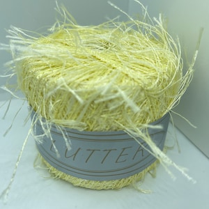 May include: A skein of pale yellow yarn with a fluffy texture. The yarn is wrapped around a cardboard tube with a gray label that reads "LUTTER".