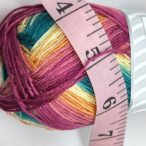 May include: A ball of multi-coloured yarn with a pink measuring tape wrapped around it. The yarn is a mix of teal, yellow, orange, and pink. The tape reads "60 inch" and has numbers 4, 5, 6, and 7 visible.