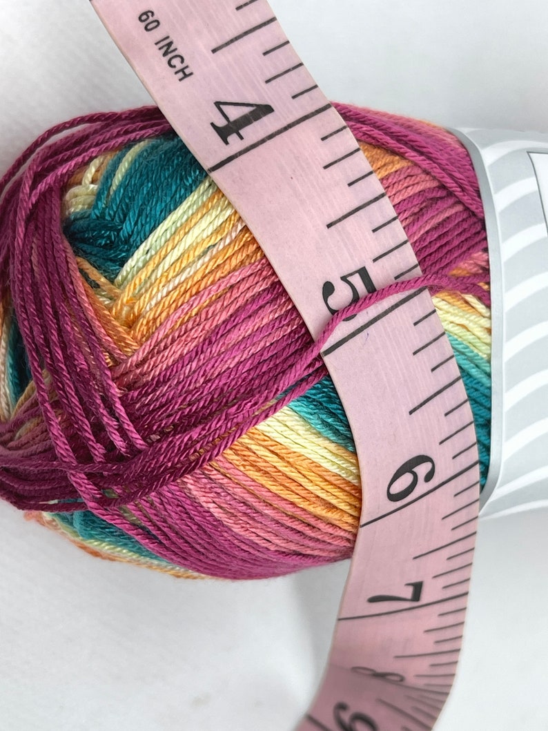 May include: A ball of multi-coloured yarn with a pink measuring tape wrapped around it. The yarn is a mix of teal, yellow, orange, and pink. The tape reads "60 inch" and has numbers 4, 5, 6, and 7 visible.