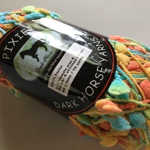 Puede incluir: Un ovillo de hilo multicolor llamado "Pixie" de Dark Horse Yarns. El hilo es 100% nylon y viene en una variedad de colores, incluyendo amarillo, naranja, azul y verde. El hilo pesa 50 gramos y tiene 76 yardas.