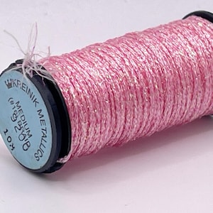 May include: A spool of Kreinik medium metallic thread in a bright pink color with a shimmering finish. The black plastic spool features a light blue label printed with the text Kreinik Metallics, Medium, #16, 9208, and 10M.