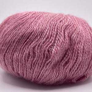 May include: A ball of dusty rose yarn, tightly wound and textured. The yarn appears soft and fluffy, ideal for knitting or crocheting projects. The color is a muted pink, suitable for various craft projects.