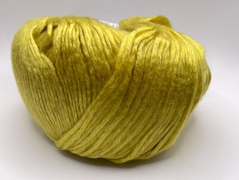 May include: A single ball of vibrant chartreuse yarn with a distinct sheen and smooth, continuous strands. The yarn is wound into a rounded, compact shape, showcasing the bright yellow-green color and the reflective quality of the fiber texture.