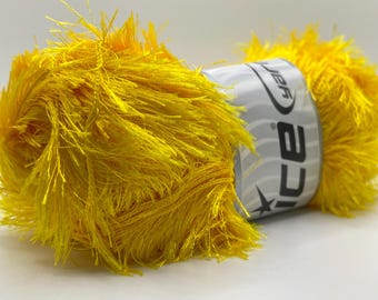 May include: A close-up shot of a bright yellow yarn ball. The yarn has a fuzzy, textured appearance. A white label with black text and a star design wraps around the center of the ball. The yarn is likely used for knitting or crocheting projects.