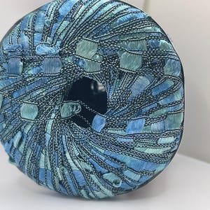 Puede incluir: Una bola de hilo de color azul y verde. El hilo está hecho de un hilo fino y delicado y tiene un acabado brillante.