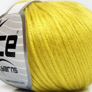 May include: A ball of bright yellow yarn wrapped with a silver and white paper label featuring the text ICE YARNS and a star graphic. The yarn has a smooth, slightly shiny texture and is wound into a compact, rounded shape for crafting projects.