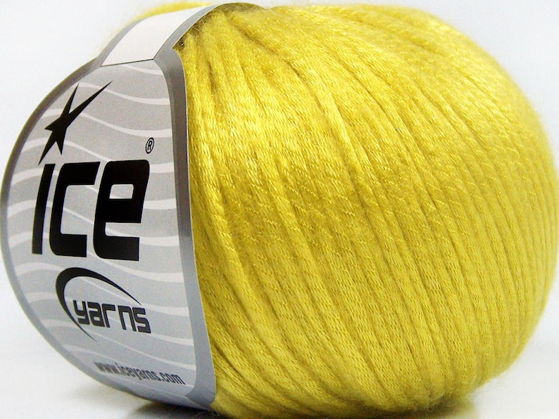 May include: A ball of bright yellow yarn wrapped with a silver and white paper label featuring the text ICE YARNS and a star graphic. The yarn has a smooth, slightly shiny texture and is wound into a compact, rounded shape for crafting projects.