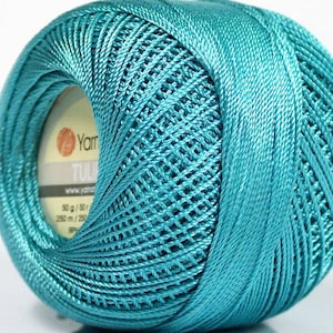 Puede incluir: Una madeja de hilo turquesa con una etiqueta que dice "YarnArt Tulip" y "50 g / 50 yds / 250 m / 275 yds".