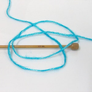 May include: A skein of turquoise blue yarn wrapped around a wooden knitting needle with the text "5.0 mm" printed on it.