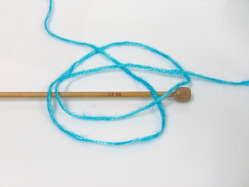 May include: A skein of turquoise blue yarn wrapped around a wooden knitting needle with the text "5.0 mm" printed on it.