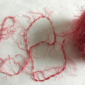 Peut inclure: Une pelote de fil rose et blanc duveteux avec un long brin du même fil disposé en forme de cœur lâche.