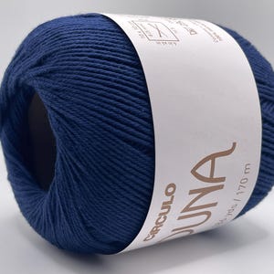 May include: A ball of navy blue yarn with a white label wrapped around it. The label features the word "DUNA" and other text. The yarn is tightly wound and appears soft, suitable for knitting or crochet projects.
