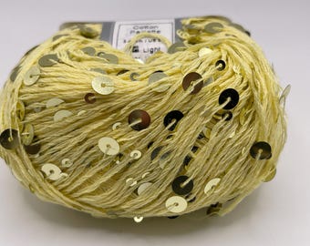 May include: A ball of light yellow cotton yarn adorned with gold sequins. The yarn is labeled "Cotton Palette" and "Light". The sequins are evenly spaced throughout the yarn, adding a touch of sparkle. Ideal for crafting projects.