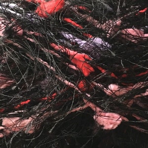 May include: Close-up of a black, pink and red yarn with a fuzzy texture.