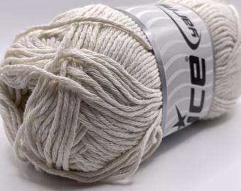 May include: A ball of off-white yarn with a label wrapped around it. The yarn is tightly wound, showing the texture of the individual strands. The label has the word "CA" and a star design.