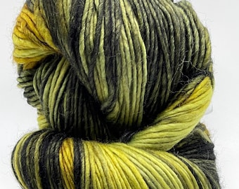 May include: A skein of hand-dyed yarn in shades of yellow, black, and green. The yarn is thick and textured, with a variegated color pattern. The colors blend together to create a unique and eye-catching effect, perfect for knitting or crocheting projects.