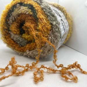 Może przedstawiać: Motka włóczki w odcieniach brązu, żółtego i zielonego. Włóczka jest puszysta i ma fakturowany wygląd.