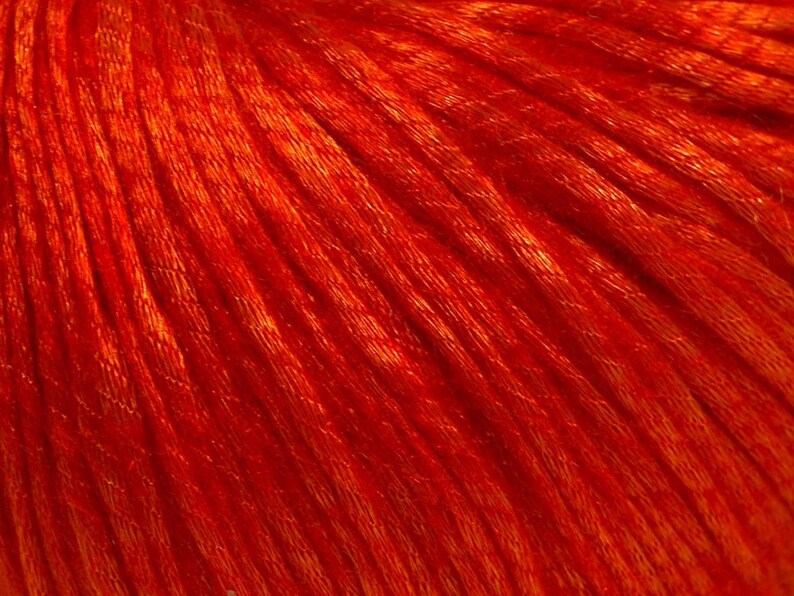 Puede incluir: Primer plano de hilo naranja vibrante, que muestra la textura y los hilos individuales. El hilo parece suave y tiene un ligero brillo, lo que sugiere un material de alta calidad. El color es un tono rico y c&aacute;lido, ideal para proyectos de tejido o ganchillo.
