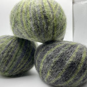 May include: Three balls of yarn in shades of green and gray are stacked on top of each other. The yarn has a textured, striped appearance. The balls are round and appear to be made of wool or a similar fiber.