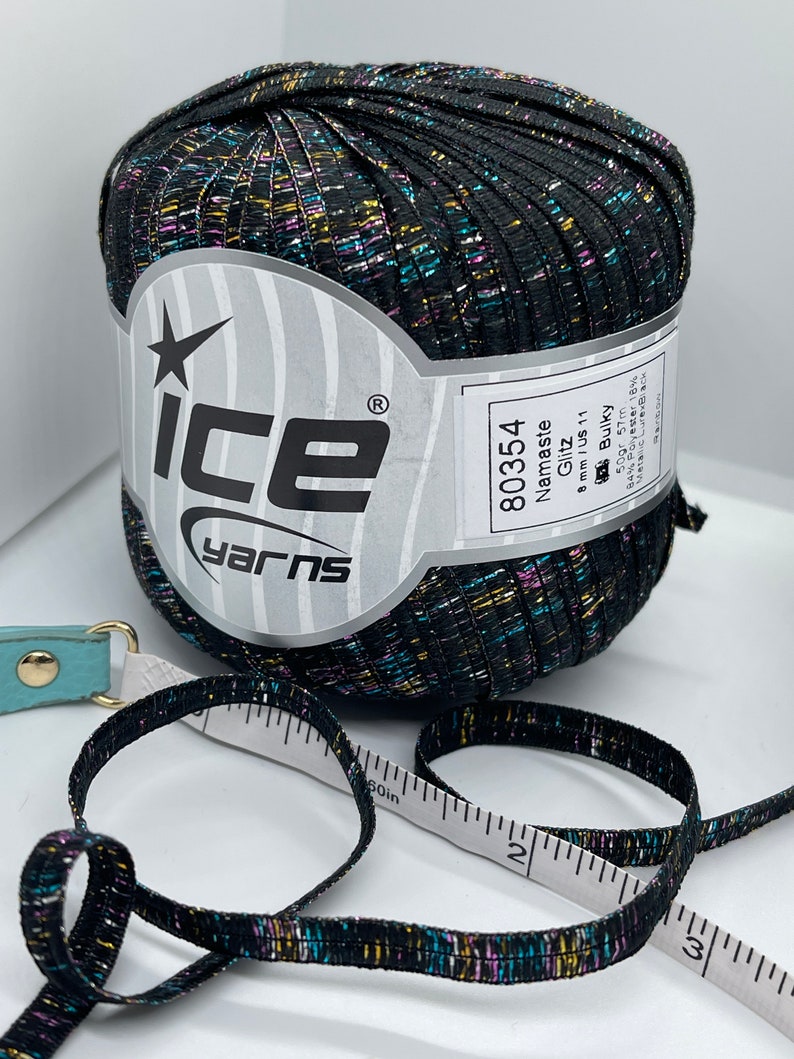 May include: A black ball of yarn with multicoloured glitter threads. The label reads "Ice Yarns", "Namaste Glitz", "80354", "8mm/US 11", "Bulky", "50gr 57m", "84% Polyester 18% Metallic Lurex Black".