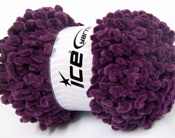 Könnte beinhalten: Nahaufnahme eines Knäuels lila Garns. Das Garn ist dick und strukturiert, mit einem weichen, plüschigen Aussehen. Das Etikett trägt die Aufschrift "ice yarns" mit einem Sternlogo. Ideal für Strick- und Häkelprojekte.